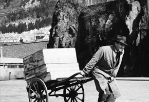 Svart-hvitt bildet av mann med fiskekasser på kjærre.