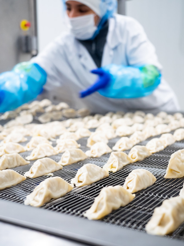 A woman with a mask and a sheet in the background, in front and focus are the gyozas