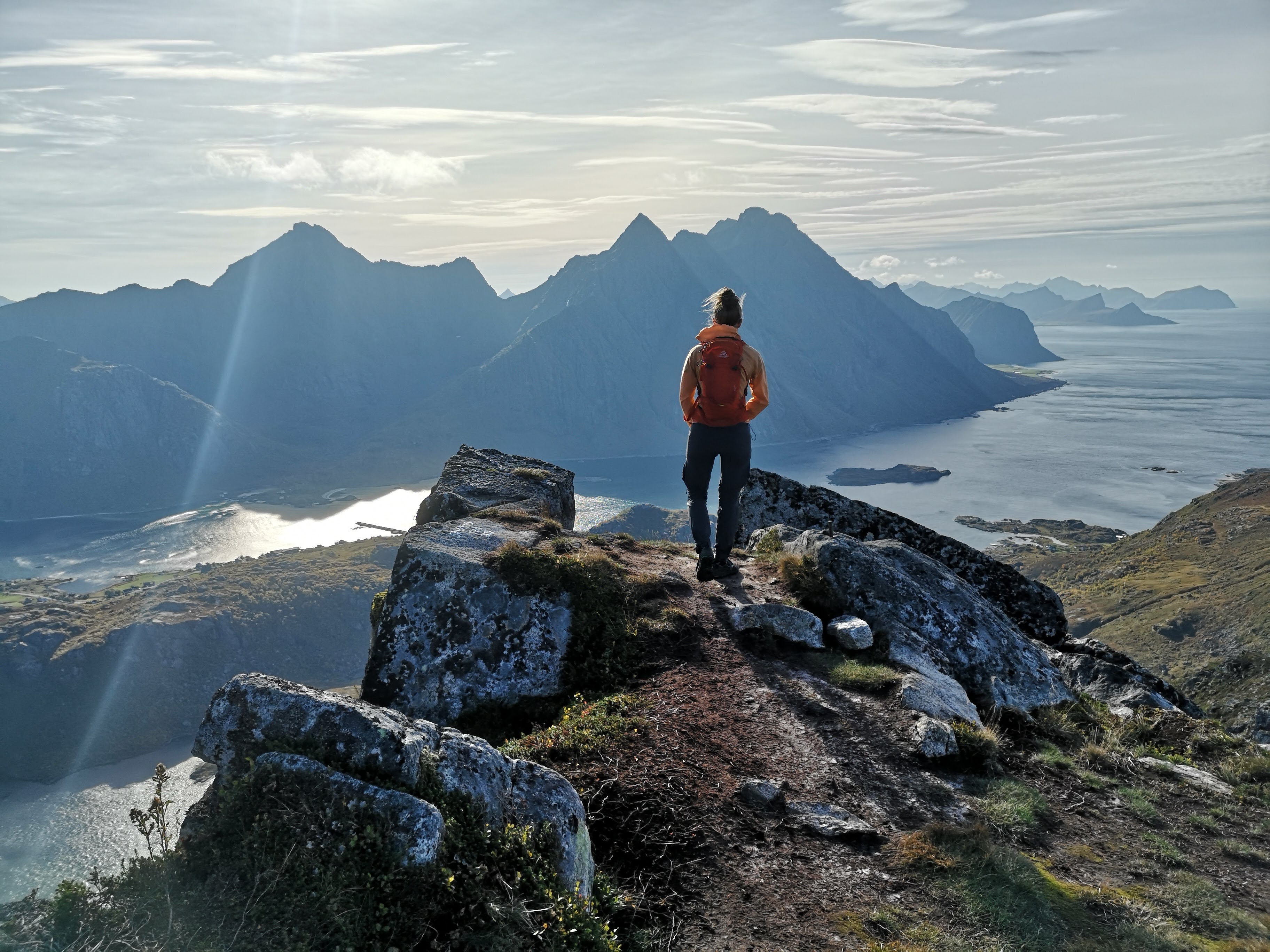Astrid on a mountain top looking at the view and landscape beneath her. Her back is turned away from the camera. 