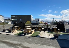 Flatt område med sittegruppe, og diverse. I bakgrunnen ser man en firkantet fabrikk med Lerøy-logo. Det er fint vær og nesten skyfri himmel